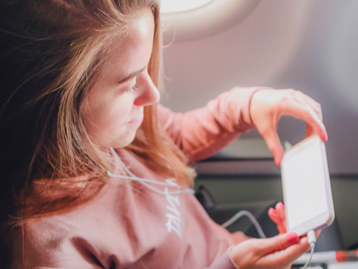Girl in pink sweater holding smartphone in airplane seat.