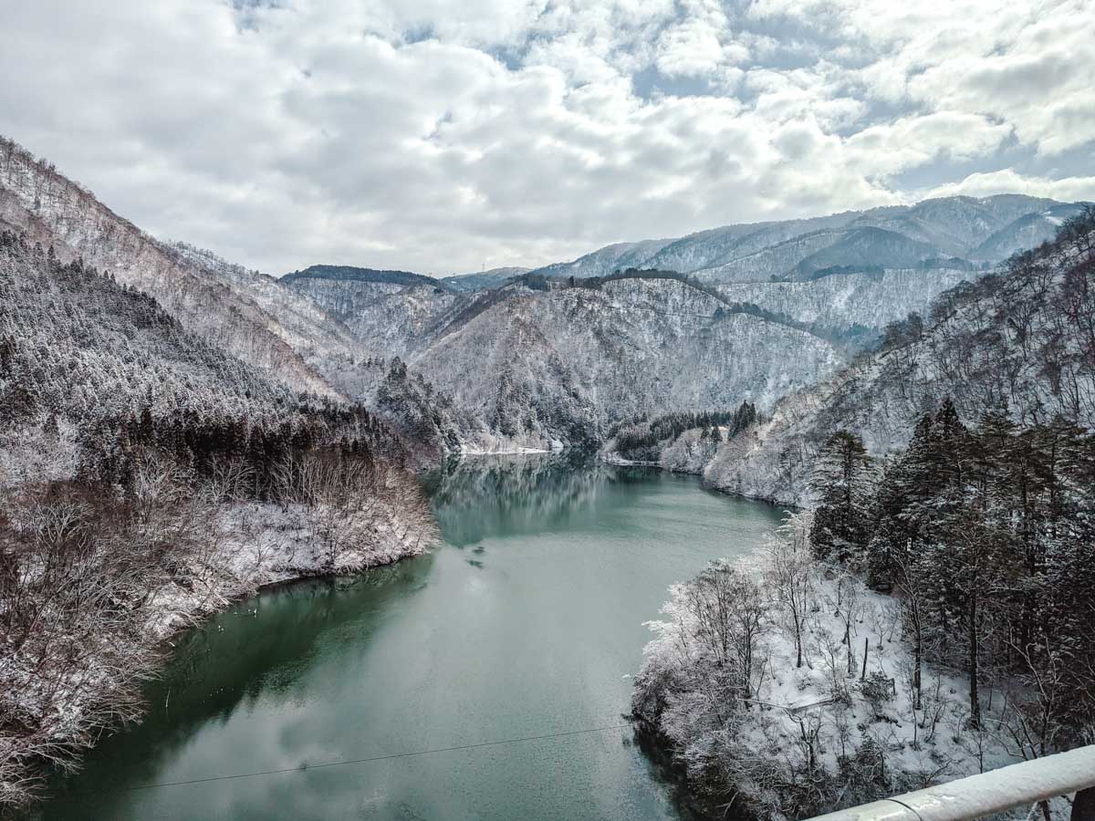 View of river flowing between two snowy mountains as seen during Kanazawa to Shirakawago day trip drive.