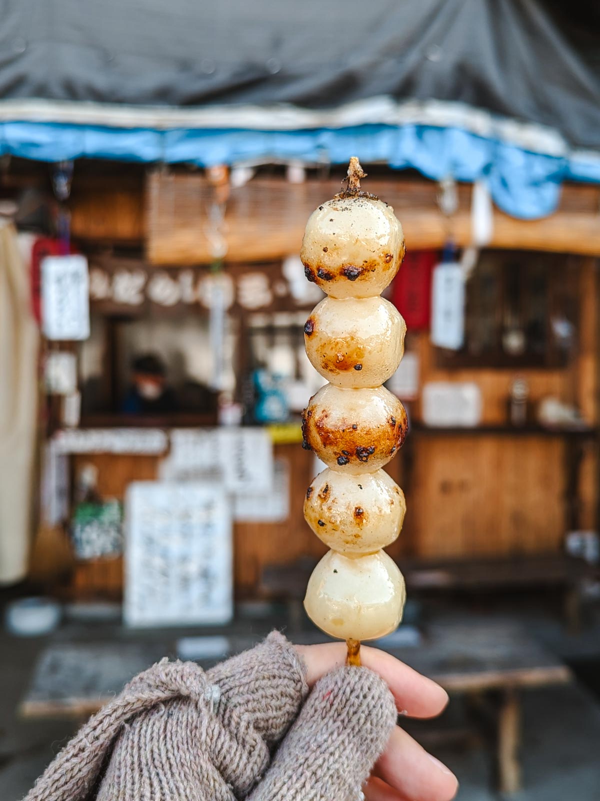 Close up view of hand holding skewer of mitarashi dango, round rice balls with brown syrup.