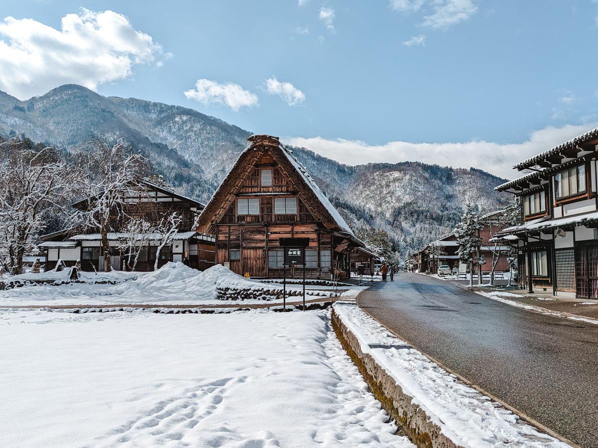 View down Shirakawago main street with large Gassho house and traditional Japanese buildings covered in snow.