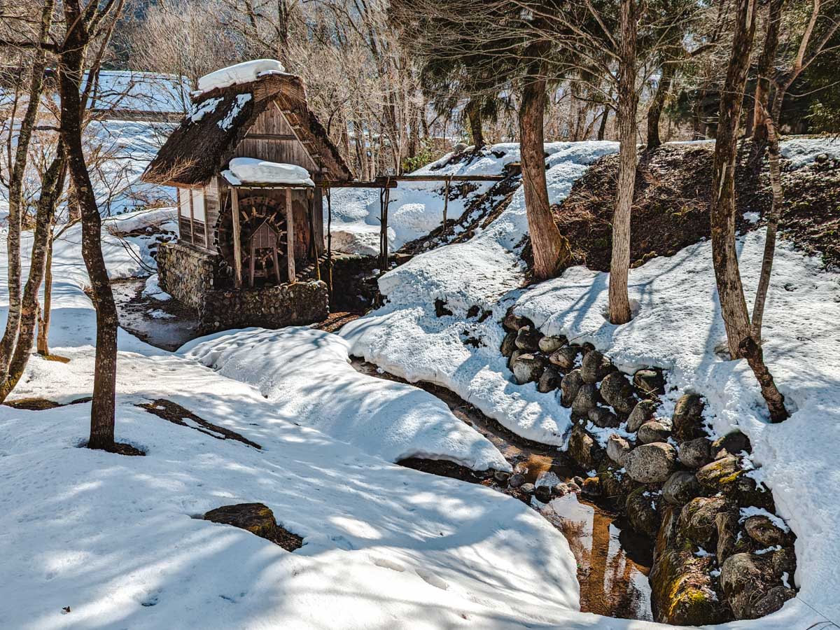 Small stream leading to old water wheel inside Shirakawago open air museum, all covered in snow.