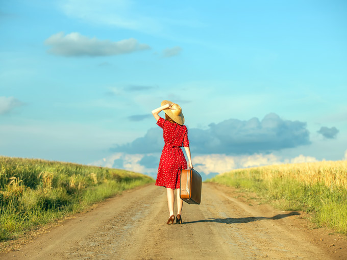 A woman starting a new life abroad with suitcase walking down dirt road.