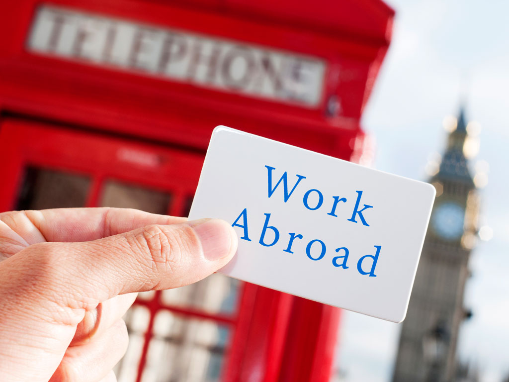 Hand holding sign that says "work abroad" in front of red phonebox.