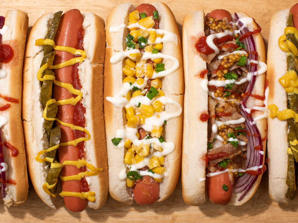 Close-up of hot dogs in buns with assorted toppings.