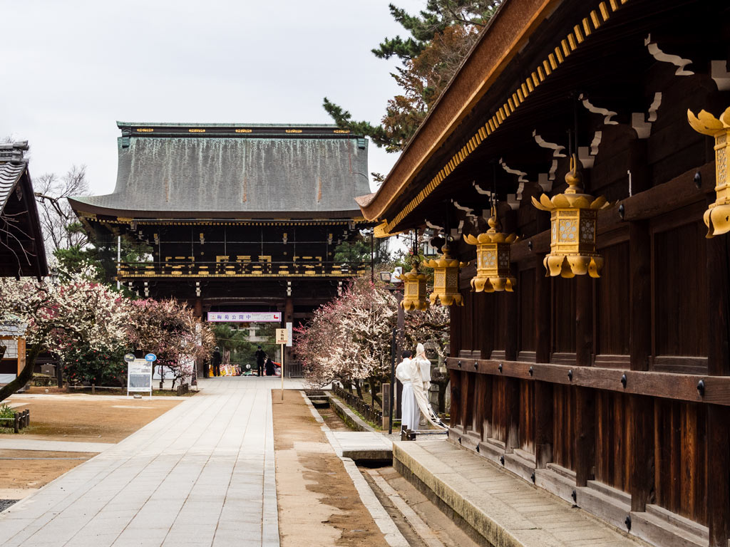Kitano Tenmangu shrine in Kyoto with gold lanterns hanging from old wooden building.