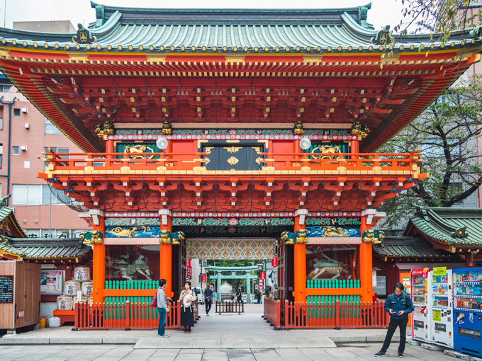 Ornate carved wooden shrine gate behind vending machines and tourists doing 6 days in Tokyo itinerary.