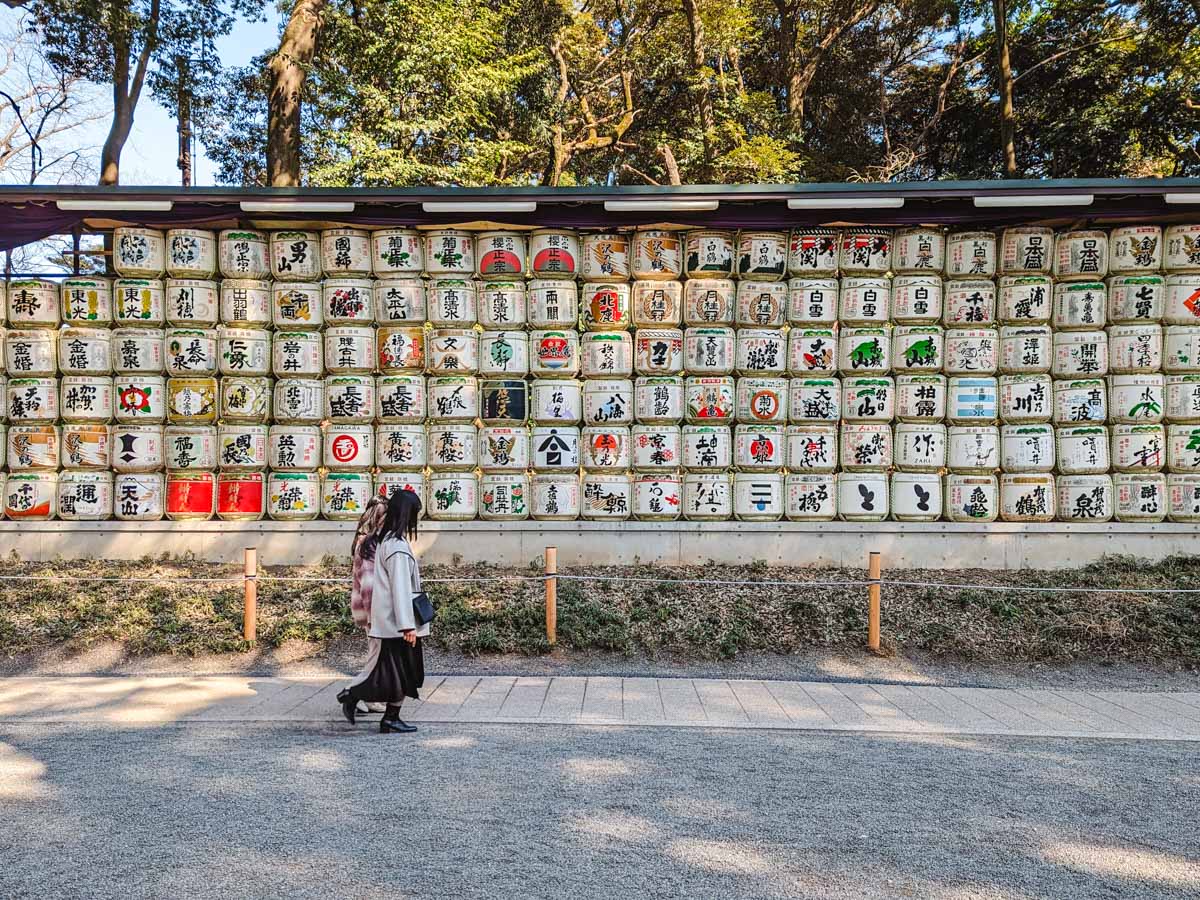 Two women walking in front of Meiji Jingu sake barrel display.