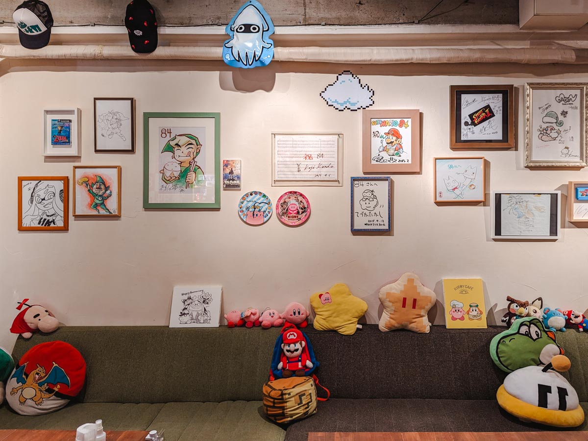 Interior of 84 Cafe secret Nintendo bar with themed plushies on seating bench and artwork lining the walls.