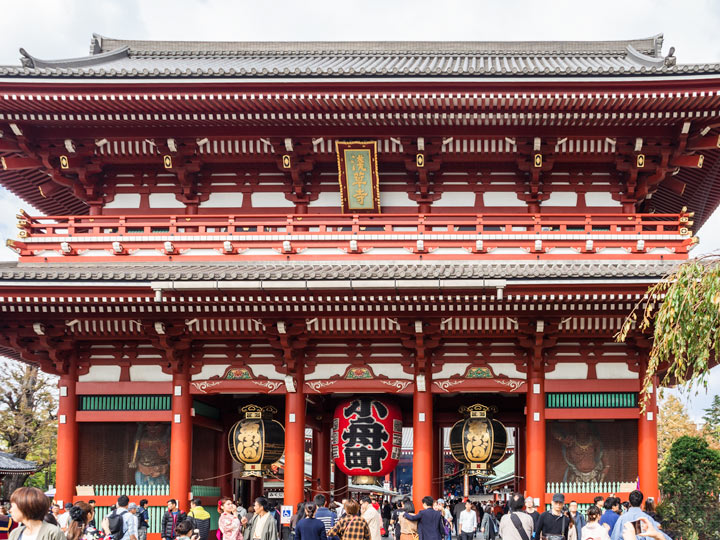 Crowd of people walking in front of Sensoji Temple with red and white facade.