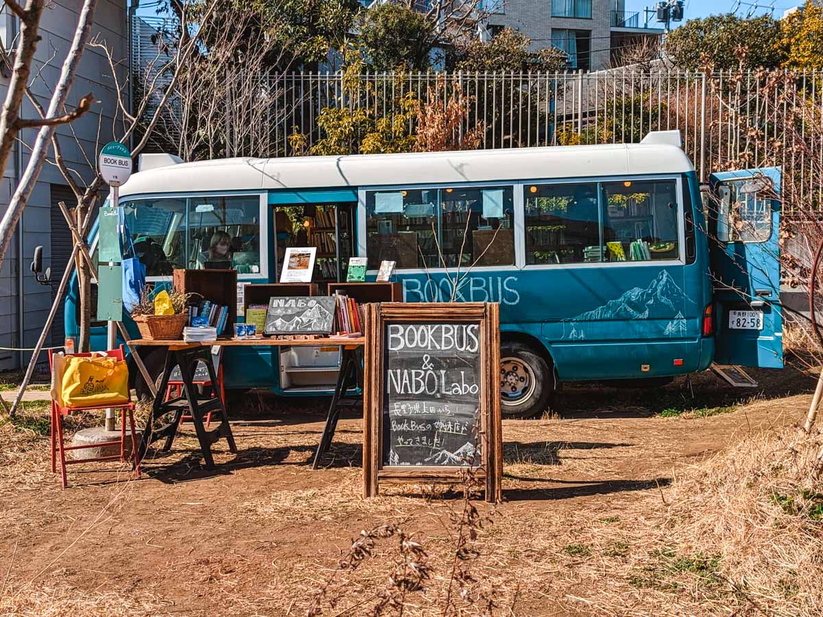 Blue vintage bus selling books parked in dirt space.