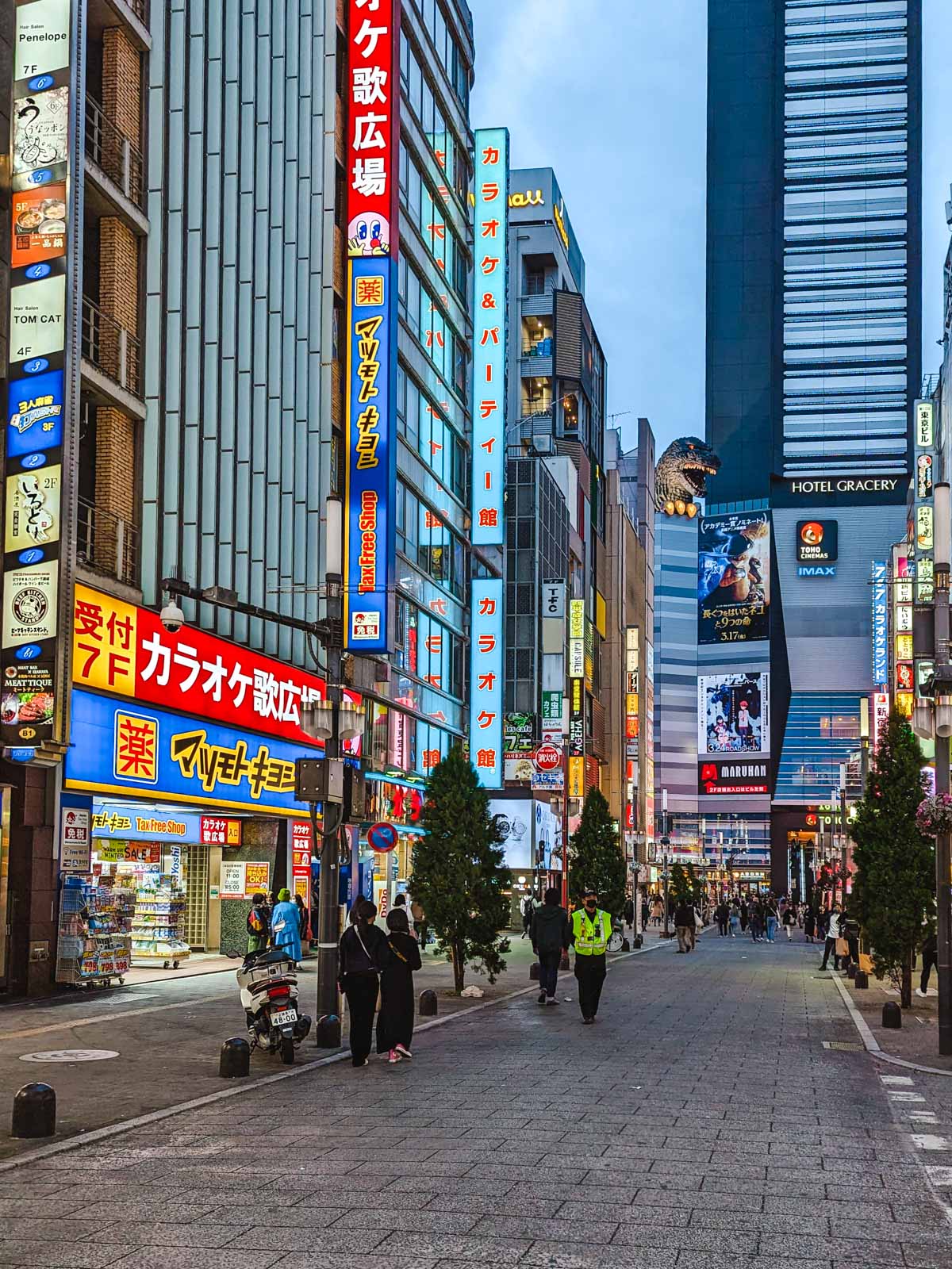 Street view of Shinjuku Tokyo at night with billboards and Godzilla statue.