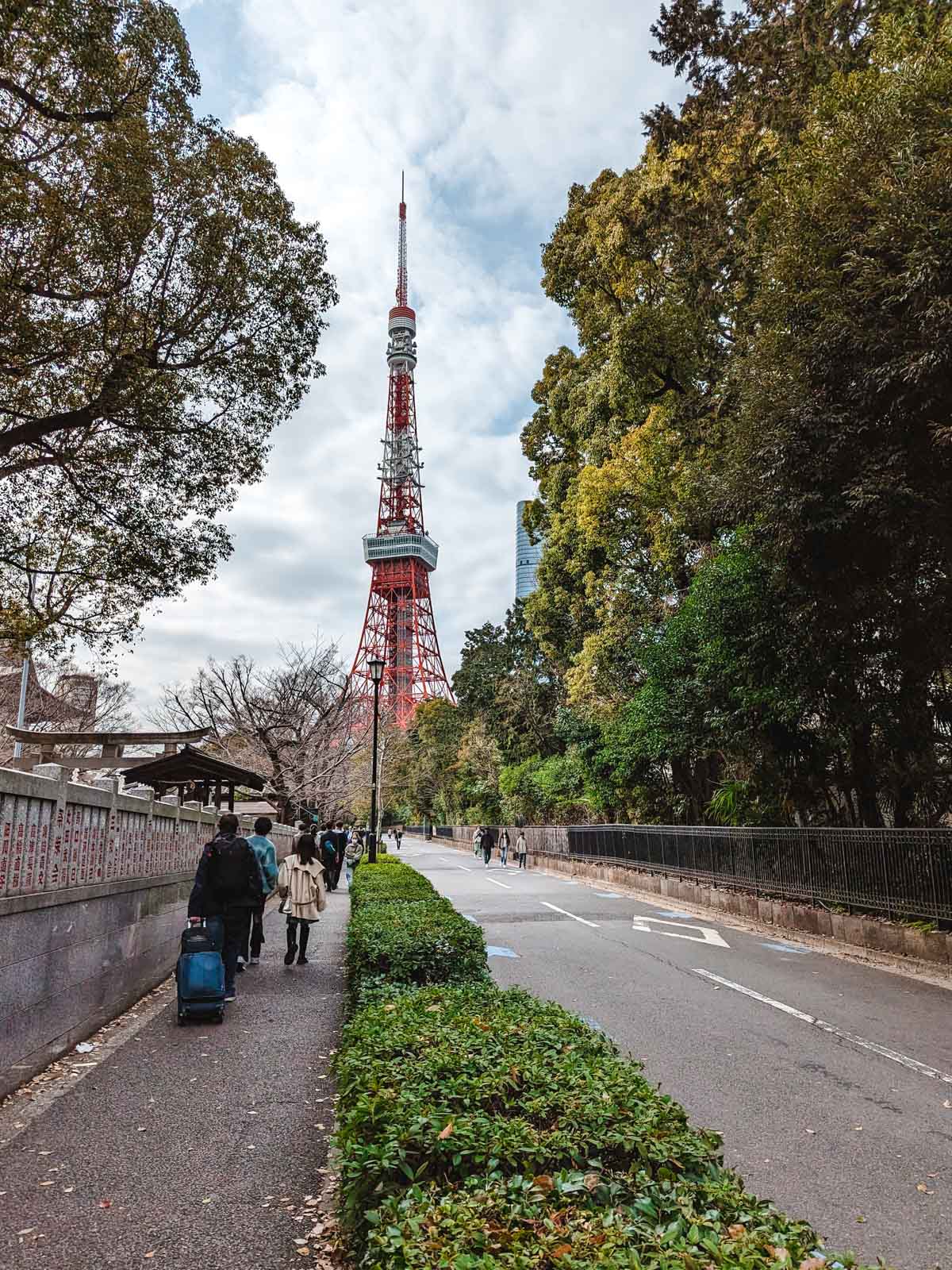 Pedestrians walking down sidewalk along street that leads to Tokyo Tower in distance.
