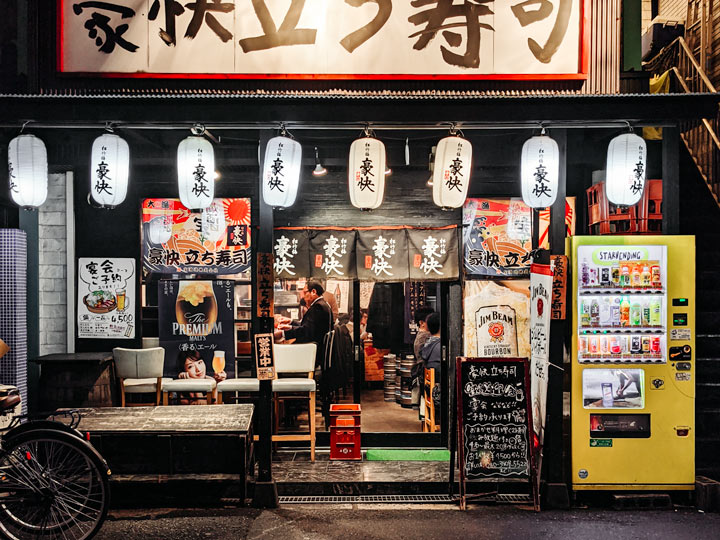 Tokyo izakaya restaurant exterior with white lanterns and vending machine.