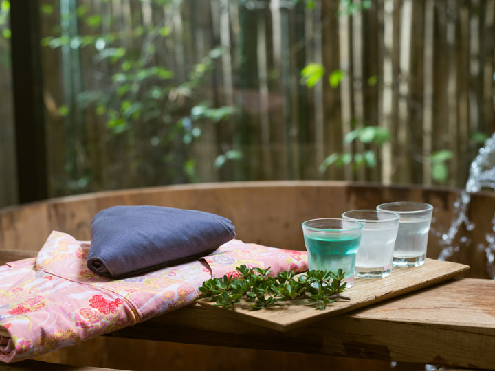 Pink yukata with three glasses on side of wooden bathtub.