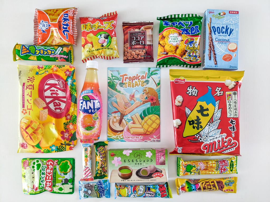 Flat lay of Japanese snacks and TokyoTreat guidebook on white table.