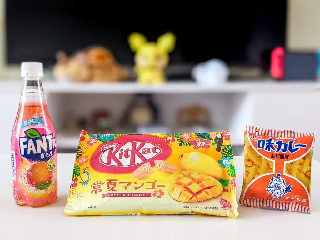 Fanta soda, mango Kit Kat bag, and curry chips bag on white table.