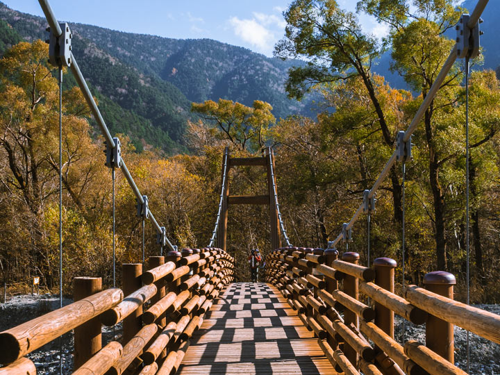 One man walking on Kamikochi bridge with autumn trees in background