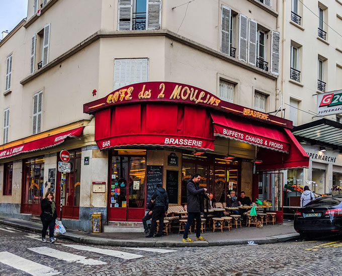 Cafe des 2 Moulins exterior with people at cafe tables eating typical French breakfast.