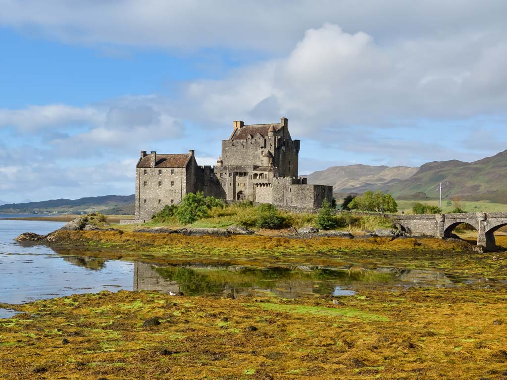 Eilean Donan castle with water and stone bridge in foreground.