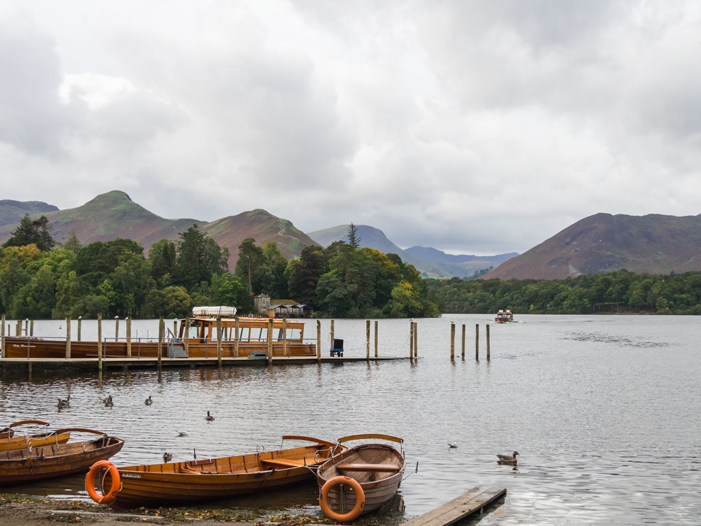 Wooden row boats pulled onto shore and dock on lake with hills in distance.