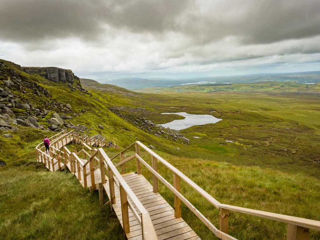 View of wooden path and green hills of Ireland's Stairway to Heaven.