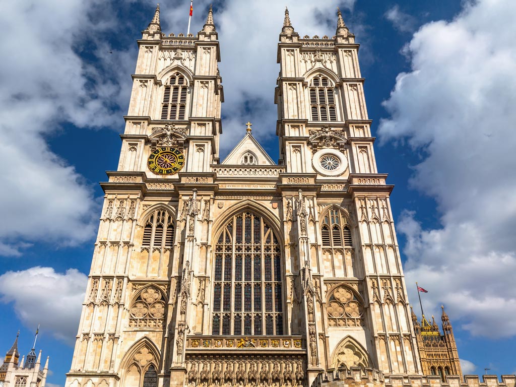 Front exterior of Westminster Abbey with two towers and stained glass windows.