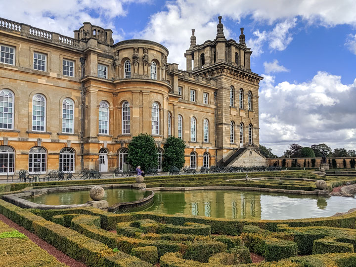 Garden hedge and pool in front of Blenheim Palace exterior.