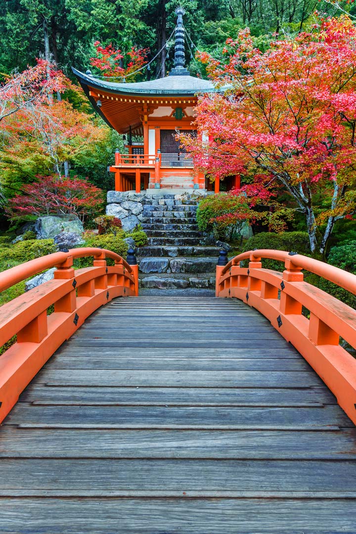 Traditional Japanese temple with orange wooden bridge leading to it.