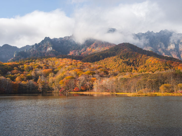 Togakushi Mirror Lake with fall foliage and white clouds.