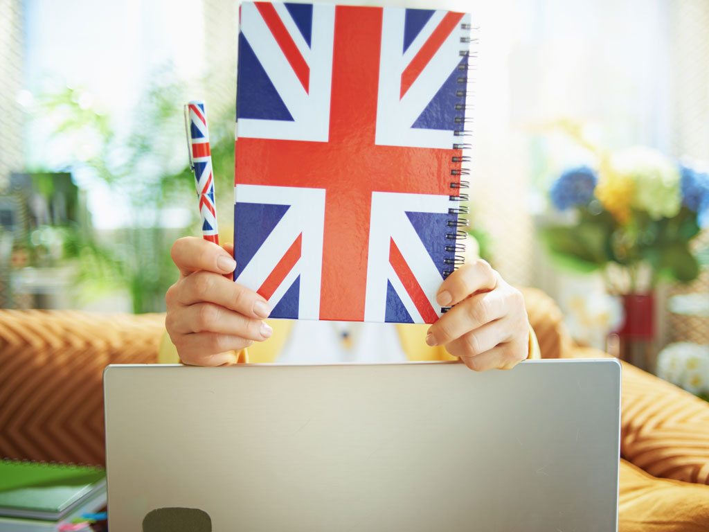 Woman holding notebook with British flag cover, reading about what is UK ILR on laptop.