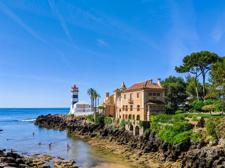 People splashing in water next to lighthouse beach during Cascais day trip.