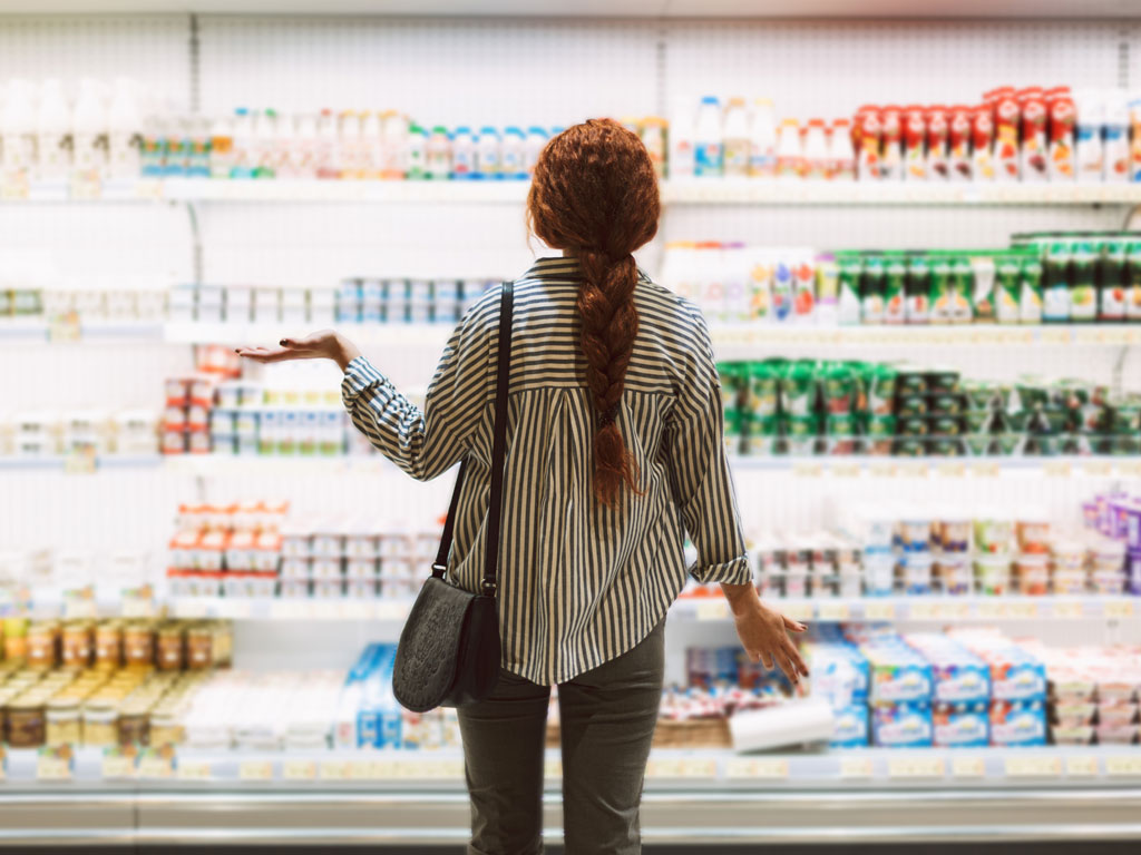 Young woman standing in front of dairy aisle wondering where to buy American food in the UK.